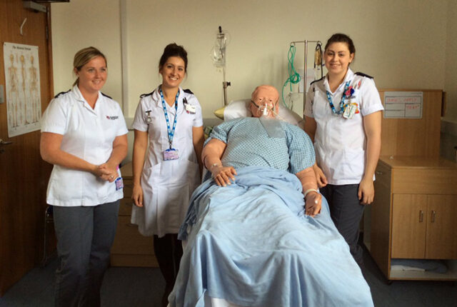 Three nursing students pose with training dummy
